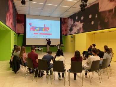 A man presenting before some 15 doctoral students sitting in a semi-circle